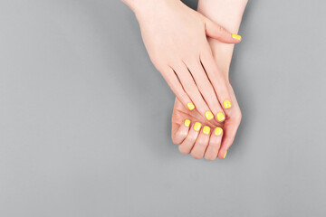 Woman hands with yellow manicure on the gray background.