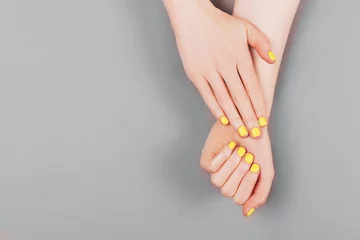 Foto op Plexiglas Woman hands with yellow manicure on the gray background. © Yulia Lisitsa