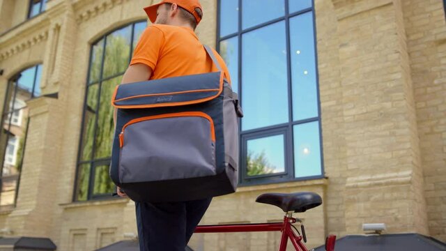 Man delivering food with bike in downtown. Courier looking for address outdoors.