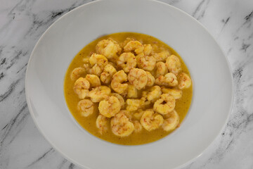Gastronomy. Seafood. Closeup view from above of cooked shrimps with a mustard and honey sauce, presented on a white deep plate on the marble table. 