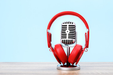 Retro microphone with red headphone put on wooden table isolated on blue pastel background.
