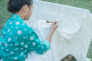 portrait young woman drawing handmade traditional batik pattern in the garden
