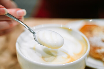 The woman's hand lifts the crema with a spoon.