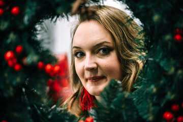 The face of a beautiful woman is looking at the camera from behind a Christmas wreath.