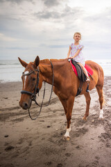Pretty little girl riding horse on the beach. Happy childhood. Sunset time by the sea. Outdoor activities. Vacation concept. Bali, Indonesia