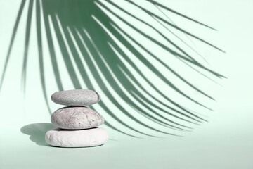 Three grey roundstones with a shadow of palm leaf on light green background. Spa stones, zen concept.Shadows photography. Eco trends. Nature aesthetic