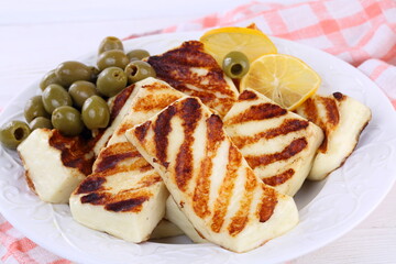 Roasted Halloumi with lemon and olives on white wooden table
