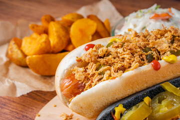American traditional fast food Hotdog with fresh organic bread bun white wheat and black charcoal sausage ketchup mustard for meal with roasted onion pickle and French fries wedges and coleslaw