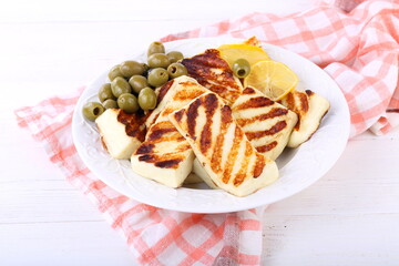 Roasted Halloumi with lemon and olives on white wooden table