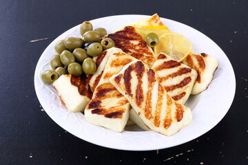 Roasted Halloumi with lemon and olives on white wooden table