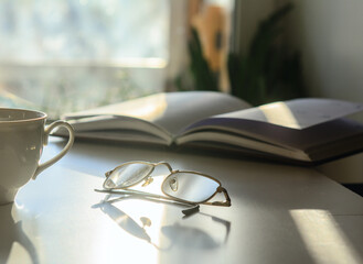In front of the window on the table are glasses, a diary and a cup of coffee. Solar illumination. Concept-work at home