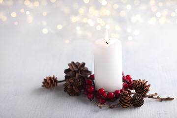 Advent candle with natural Christmas decoration and lights of garland   on white  rustic wooden  table.  Selective focus.  Focus on candle flame.