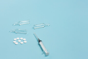 Medical ampoules, pills and syringe on the blue background. Concept of medicine and healthcare. Copy space.