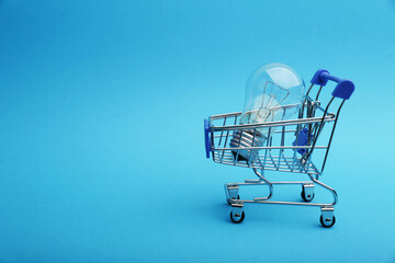 electricity purchase concept. bulb lamp in a supermarket trolley on a blue background.