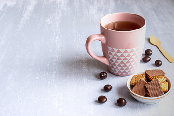 Pink cup of black tea on grey background, with cookies, chocolates and a wooden spoon. Copy space. 