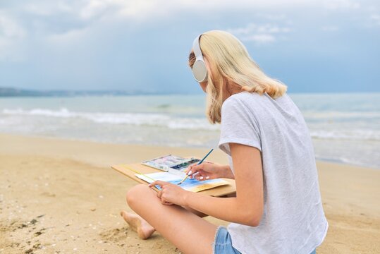 Young woman artist painting with watercolors sitting on the seashore