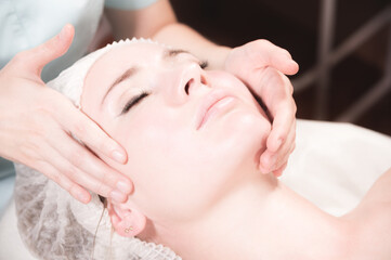 Fototapeta na wymiar Professional masseur woman making facial massage in spa salon close-up.