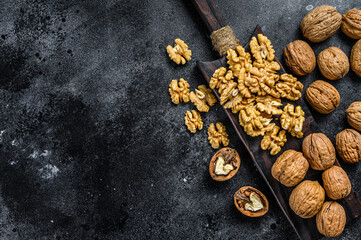 Fototapeta na wymiar Shelled walnuts kernels on wooden cutting board. Black background. Top view. Copy space