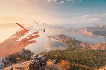 Hand holding a toy airplane on the background of the sea beach and lagoon at sunset. Concept of opening new flights in airlines and air transport