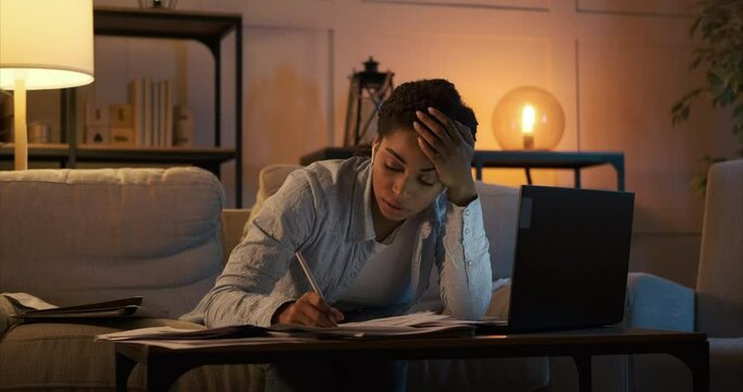 Exhausted woman writing notes while working overtime late night at home