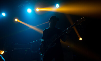 Silhouette of man play bass on Rock concert stage with colorful lighting.