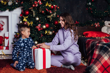 Mom and son sit by Christmas tree new year decor gifts