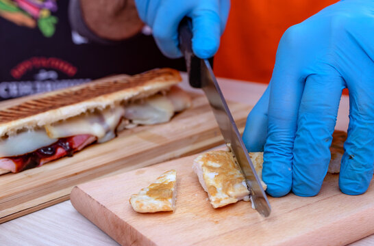 Chef preparing tasty grilled baguette submarine sandwich. Close up of hands in gloves cutting grilled chicken meat with a knife.    - Powered by Adobe