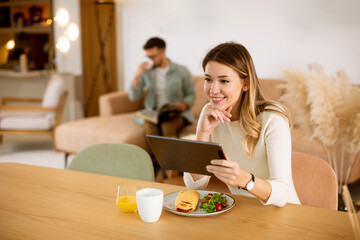 Young woman using digital tablet and having breakfast in the kitchen