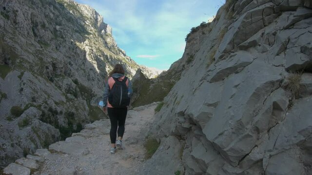 Cain, Spain - September 1, 2020: Female hiking trough the Cares Route in the heart of Picos de Europa National Park, Spain. Narrow and impressive canyon between cliffs, bridges and caves