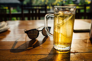 Sunny summer day. there is a big cup of beer on the table, after a high drink, sunglasses in the background