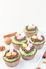 Carrot cake muffins with cream cheese frosting and Easter chocolate eggs, on white plate, vertical, copy space