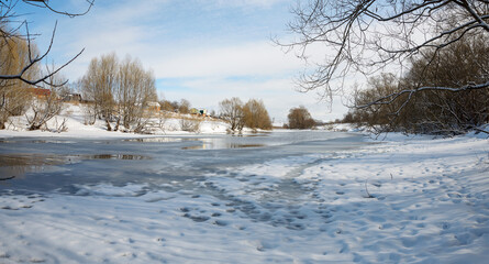 Sunny spring rural landscape with bare trees growing on the bank of river.Melting snow and ice.