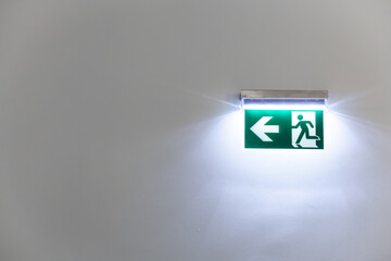 Fototapeta na wymiar green illuminated emergency exit sign on a white wall of a building