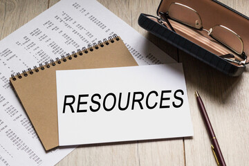 Text RESOURCES on a business card lying on a notepad with eyeglasses and text documents. Could be for business, financial and marketing concepts