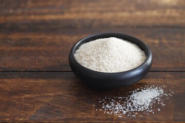 Psyllium hask in a black ceramic bowl. Dark concrete background