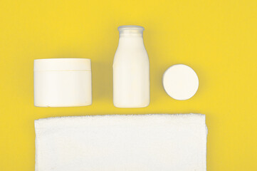 White cosmetic jars and towel on yellow background. Color 2021 illuminating. Skin care concept.