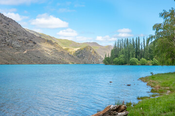 Fototapeta na wymiar Clutha River with sun on scenic grassy slopes and turquoise river under blue sky