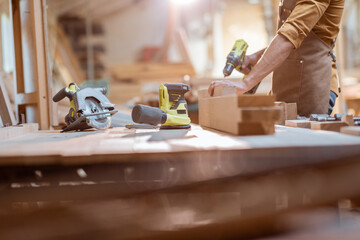 Carpenter working with modern cordless tools and wooden bars on the workbench at the workshop