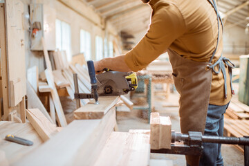 Carpenter sawing wooden bars with cordless electric saw at the joiner's workshop