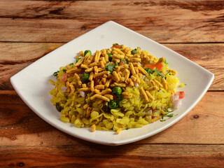 Poha, made with flattened rice, typically Western Indian breakfast, served in a plate over a rustic wooden background, selective focus