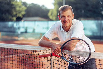 Portrait of positive male tennis player with racket standing at clay court