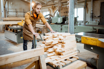 Carpentry worker pushing cart full of wooden planks at the joinery warehouse