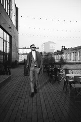 Full length body size photo of fashionable man walking outside cafe wearing plaid suit coat sunglass