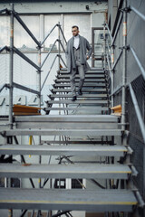 Full length body size photo of young businessman in grey coat scarf going down stairs looking at side