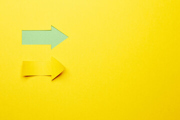 Two direct right paper arrows, one cutted from the yellow paper curved up of two sides on the yellow paper background other made as an arrow shaped hole in the background with green paper underlay