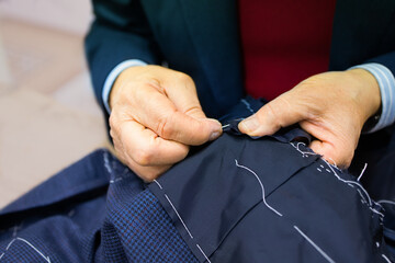 The hands of an elderly tailor basting and sewing the men's jacket. Sartorial clothes are made by...