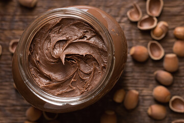 Close-up shot of chocolate-nut paste spread in glass jar on wooden background top view