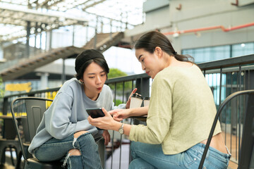 Two young woman having fun with smartphones at coffee breaks in public places. Business people using cellular mobile phone in a street cafe. 5G communication technology, internet networks concepts