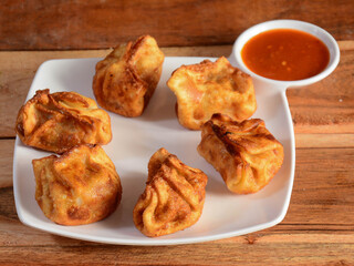 Chicken fried momo with sauce served over a rustic wooden background, selective focus