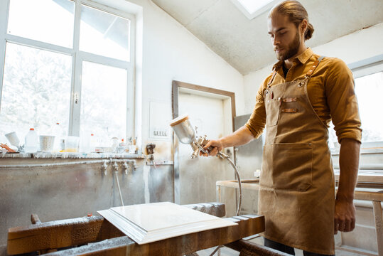 Worker painting wooden product with a spray gun at the painting shop of the carpentry